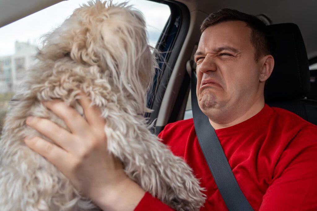 man holding up dog and grimacing due to dog's bad breath