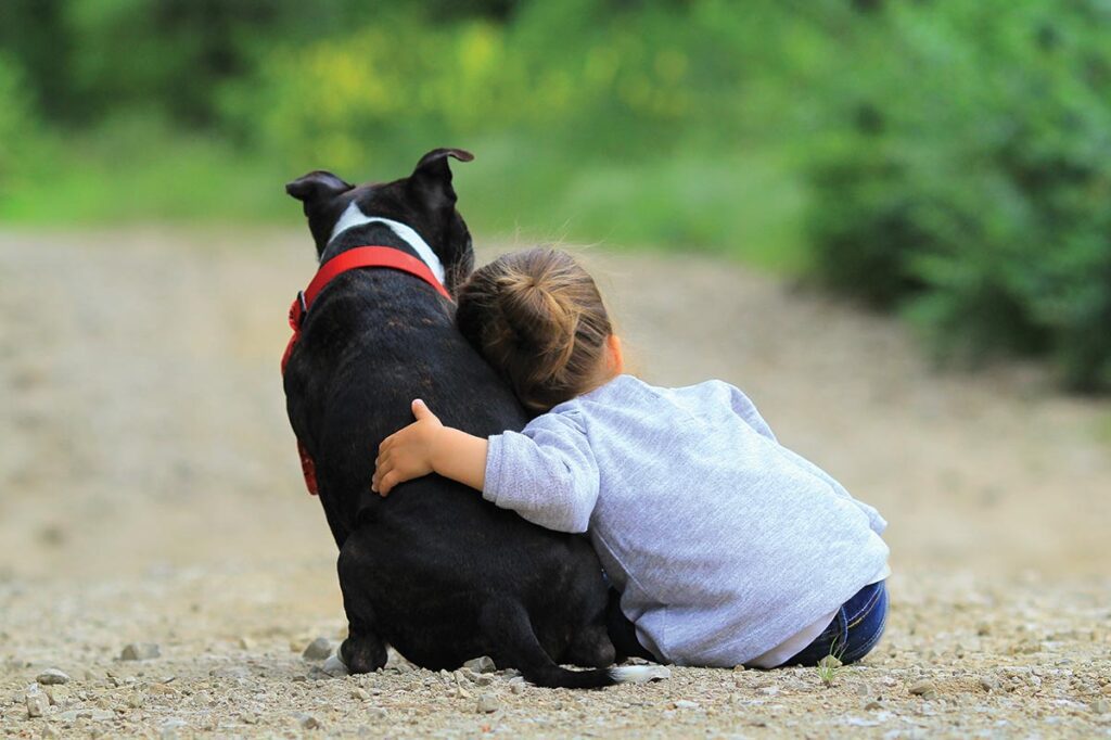 young child sitting and hugging dog outside