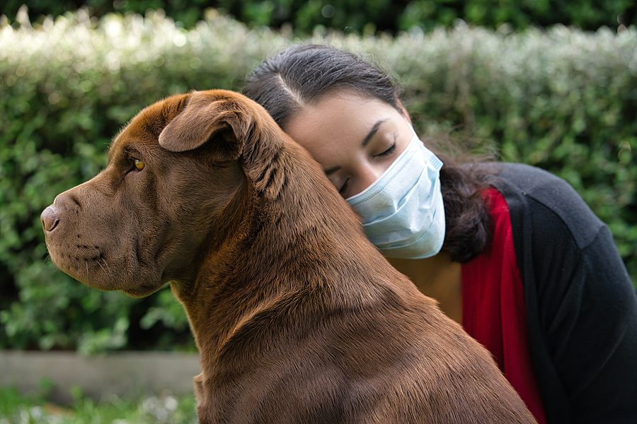 woman wearing a mask and hugging her dog outside