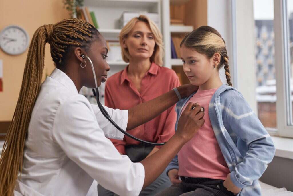 little girl getting checked out by the doctor while her mom stands next to her