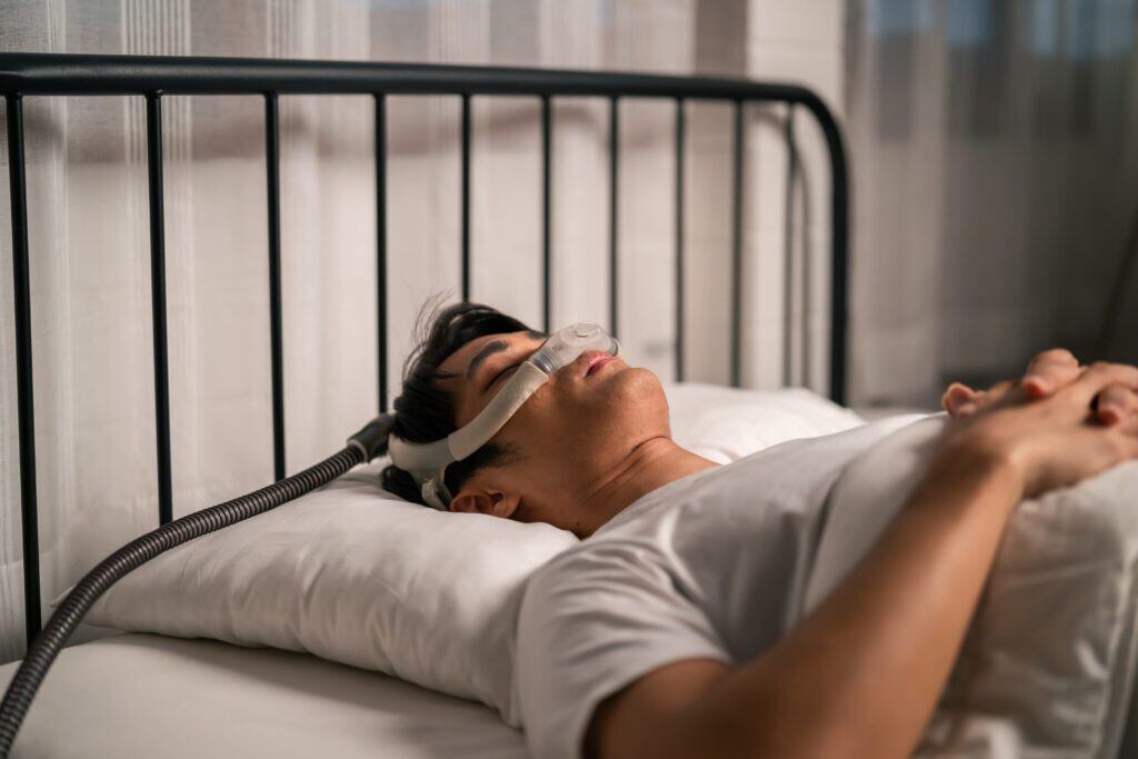 man sleeping in a bed with a sleep apnea machine on his face