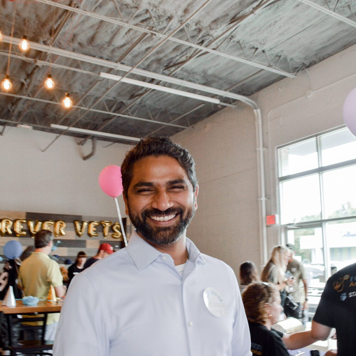 smiling man standing in room where party is happening in the background