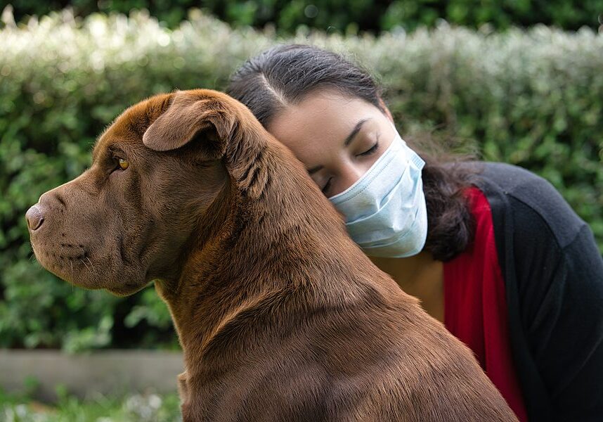 woman wearing a mask and hugging her dog outside