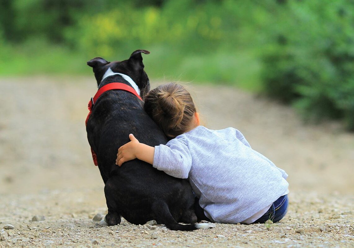 young child sitting and hugging dog outside