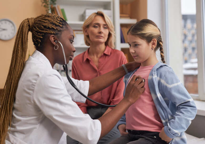 little girl getting checked out by the doctor while her mom stands next to her