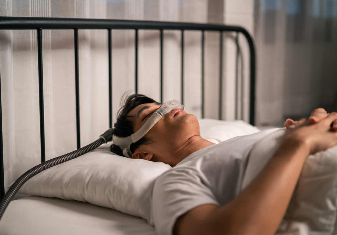 man sleeping in a bed with a sleep apnea machine on his face