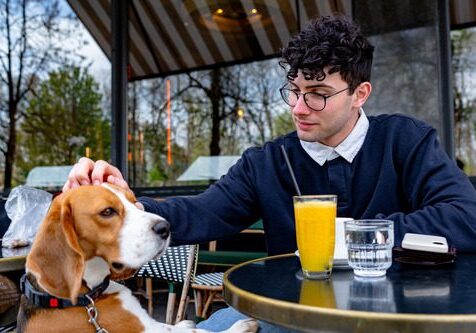 young man sitting at an outdoor table at a restaurant with his beagle dog