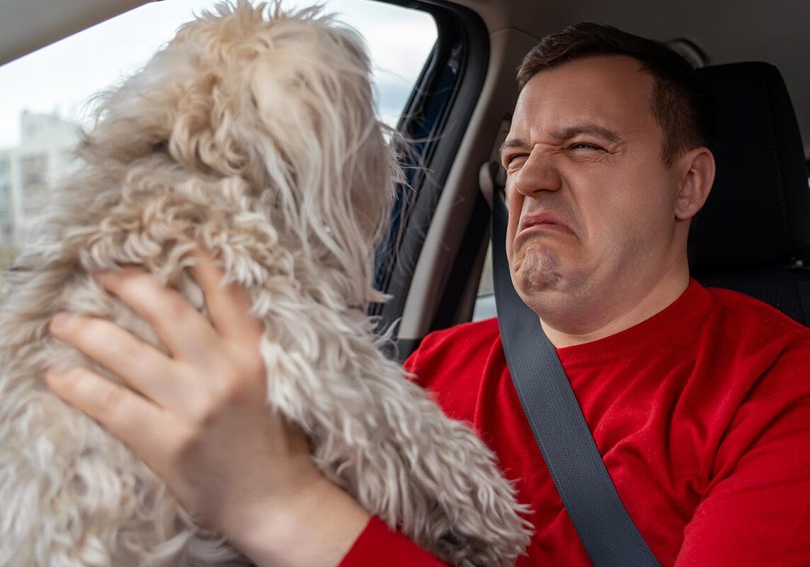 man holding up dog and grimacing due to dog's bad breath